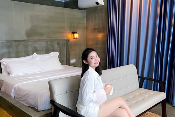 Woman sits on couch in front of bed in boutique villa at damnak borey resort in kampot
